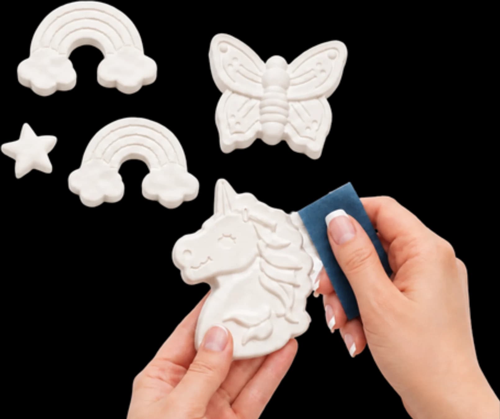 Two hands sanding a plaster unicorn, with rainbow, butterfly and star figurines waiting beside it